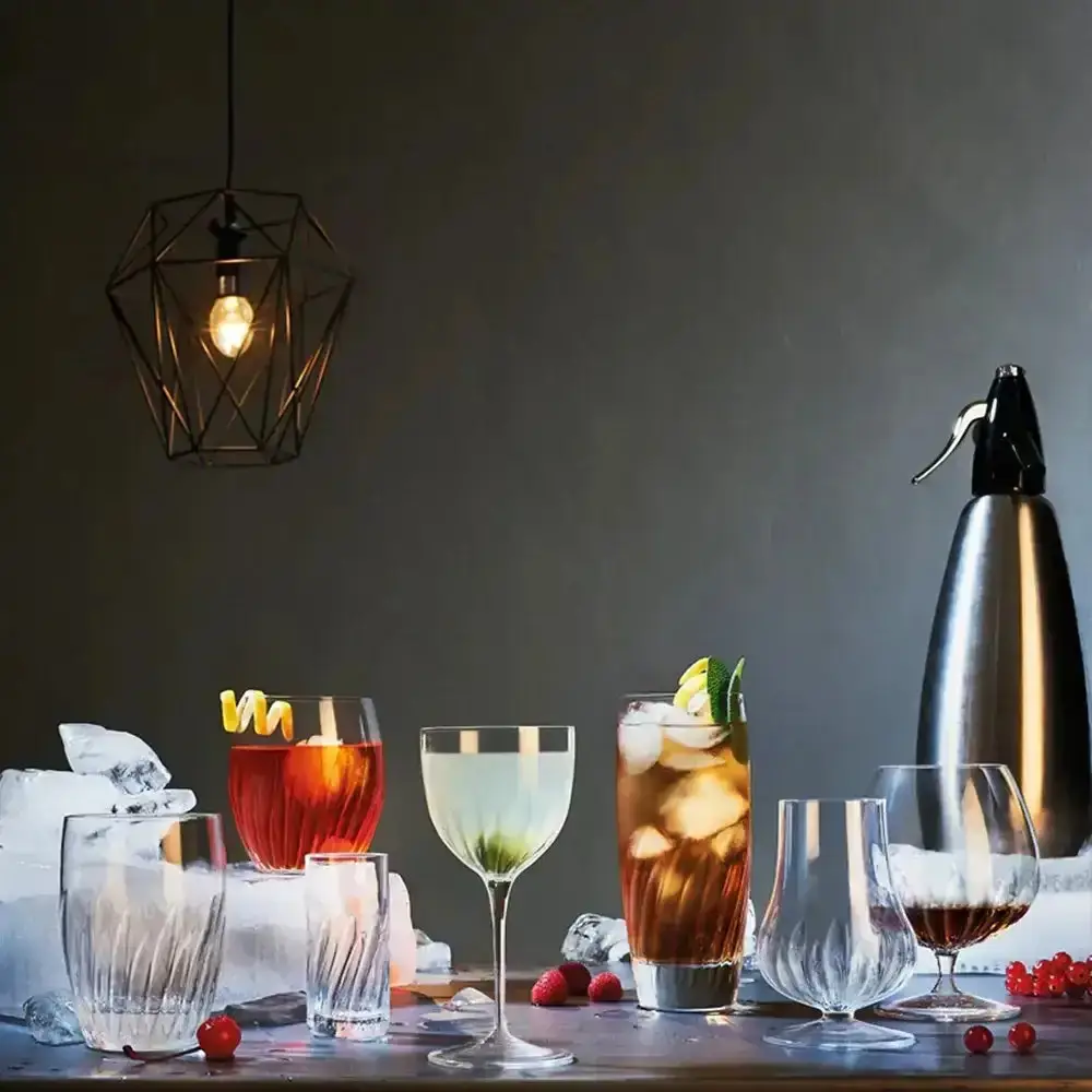 Cocktail glasses, a soda siphon and mixed drinks arranged under a geometric pendant light