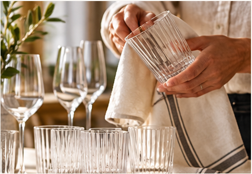 Drying a ribbed tumbler with a linen tea towel beside clean wine glasses