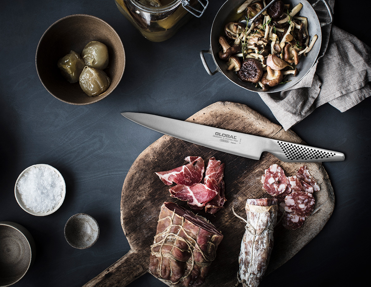 Global carving knife beside prepared roast meat on a kitchen work surface.