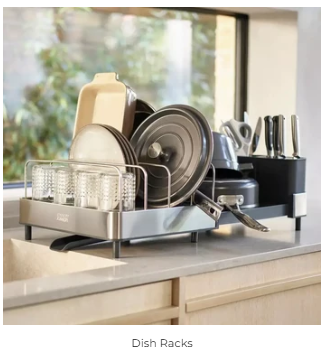 A stainless steel dish rack on a kitchen counter holding glasses, pan lids and a knife block by the window