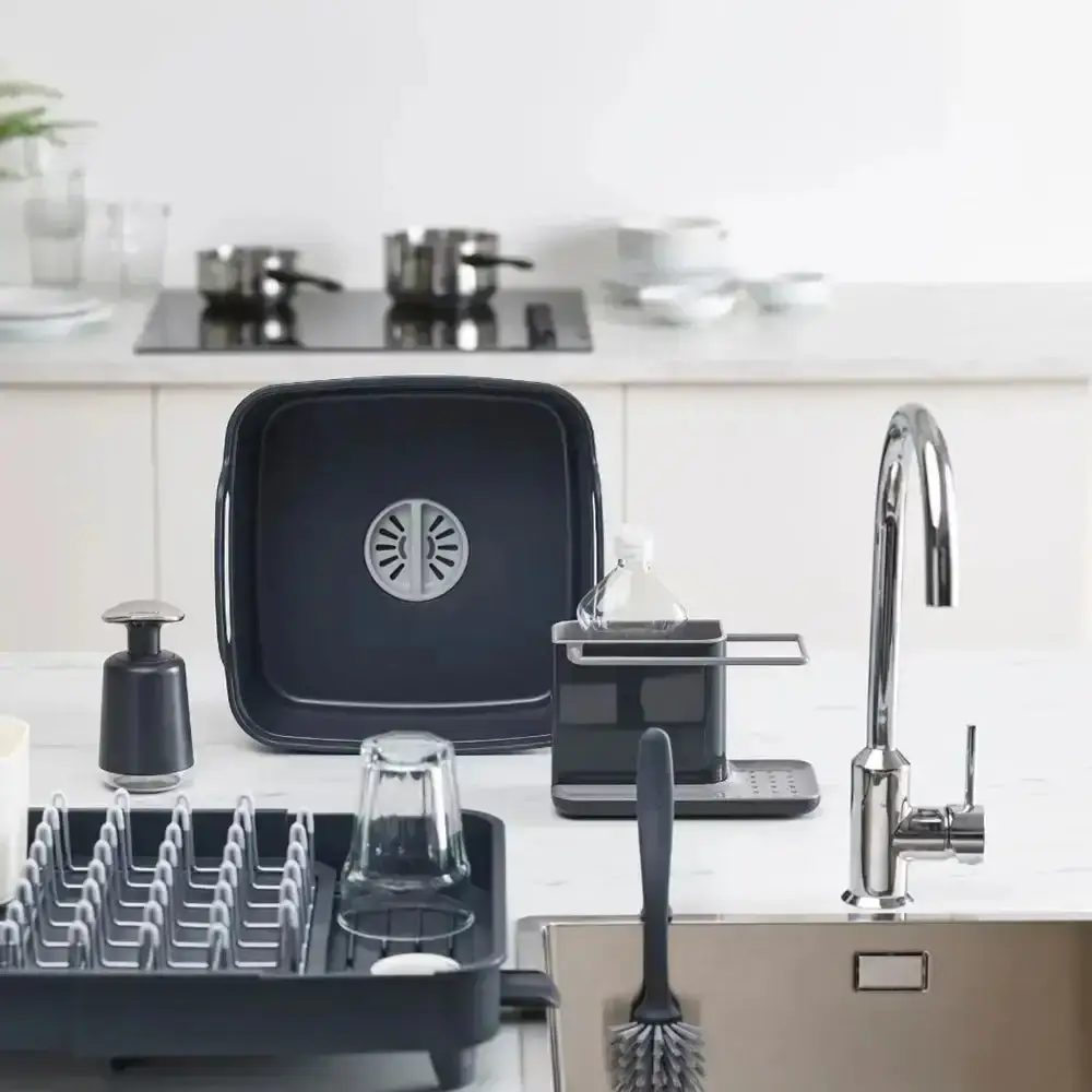 A grey sink caddy, soap pump, washing-up bowl, dish rack and sink brush arranged around a stainless steel sink
