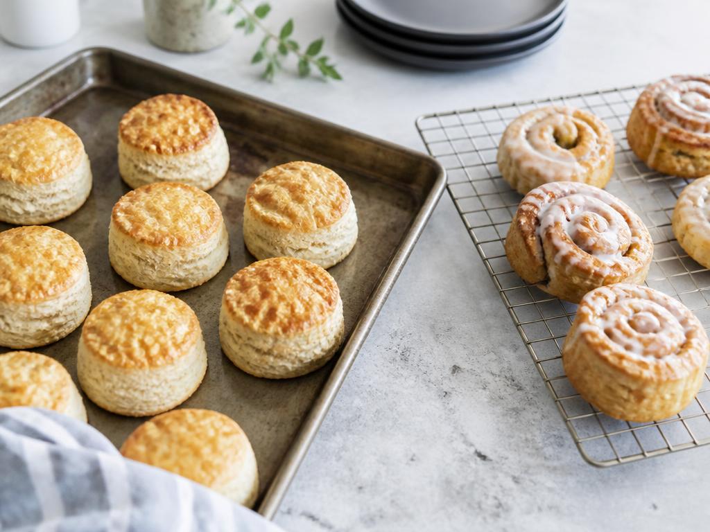 A baking sheet of golden cookies lifted from the oven above a wire cooling rack and roasting trays