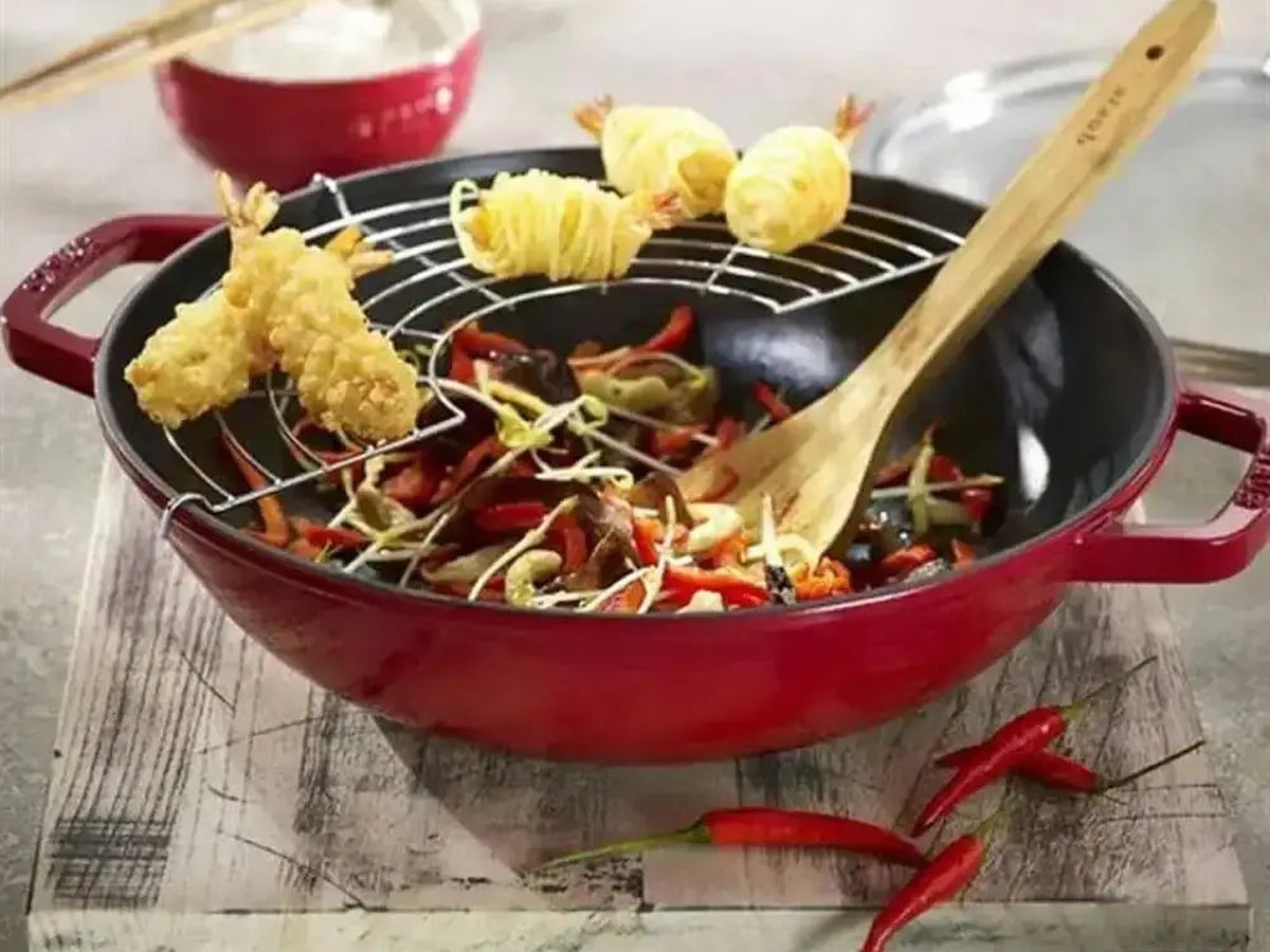 A red enamelled cast-iron wok with a tempura rack, prawns and stir-fried vegetables on a pale board