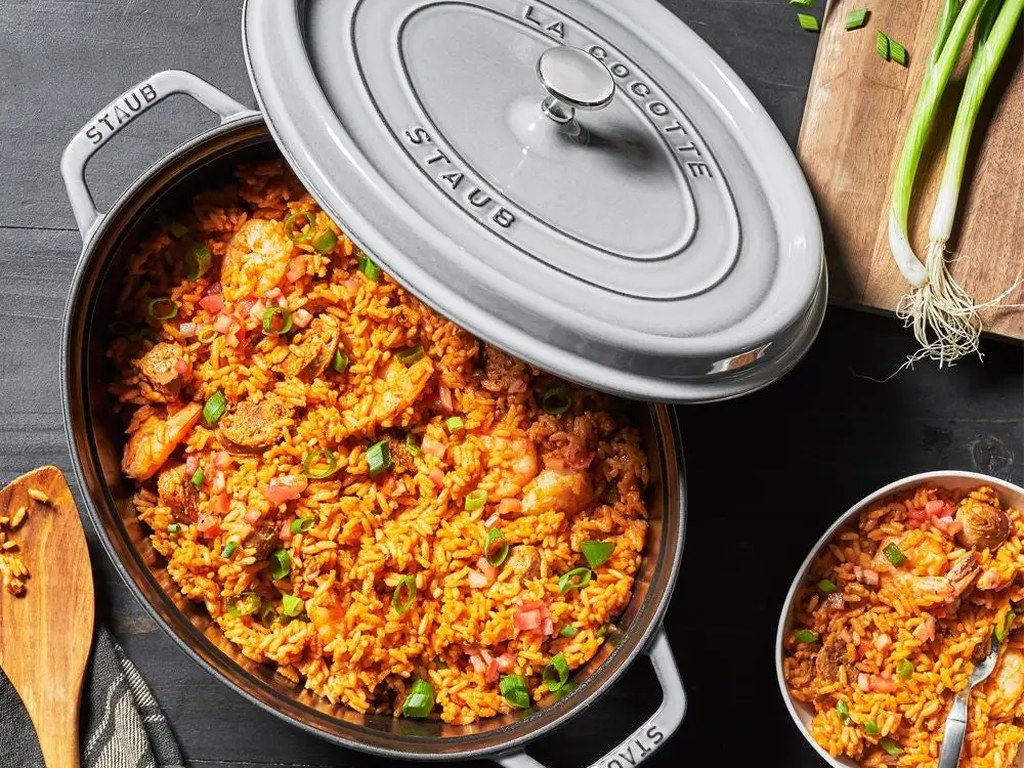 A light grey Staub casserole with the lid slightly open, filled with slow-cooked beef stew