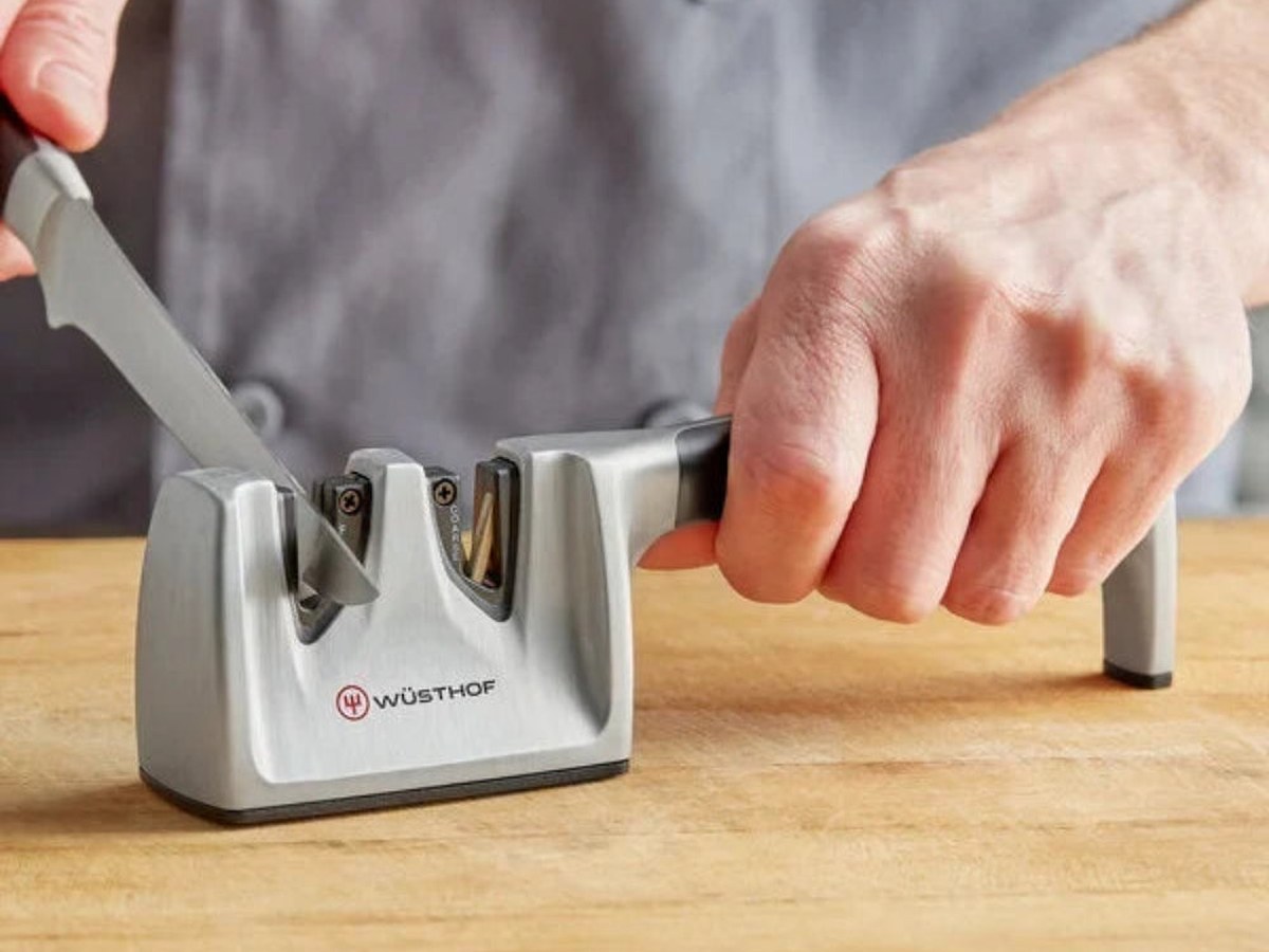 Hands drawing a chef's knife across a sharpening stone on a pale stone counter