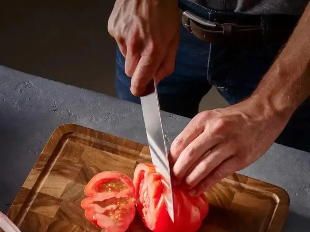 A vegetable knife cutting through fresh produce on a board in daylight
