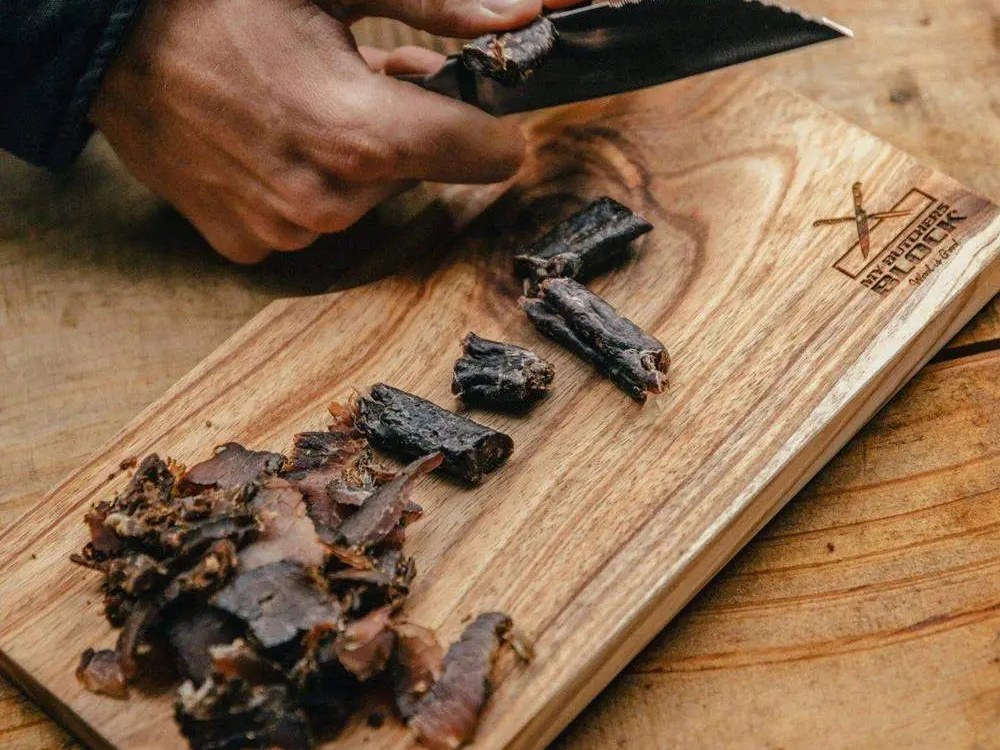 Hands slicing biltong with a knife on a My Butchers Block hardwood biltong board