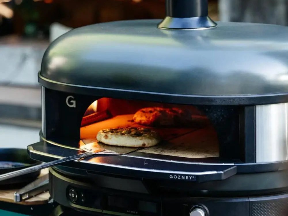 A pizza being launched into a lit Gozney Dome Gen 2 dual-fuel outdoor pizza oven