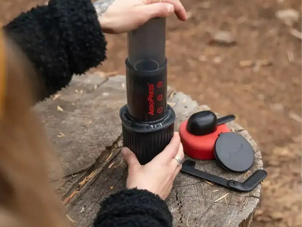 Hands pressing an AeroPress Go travel coffee maker on a tree stump outdoors
