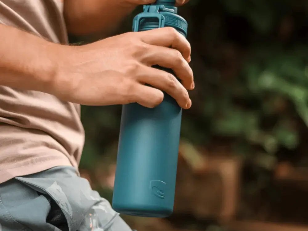 A man outdoors holding a teal Lizzard insulated stainless steel flask