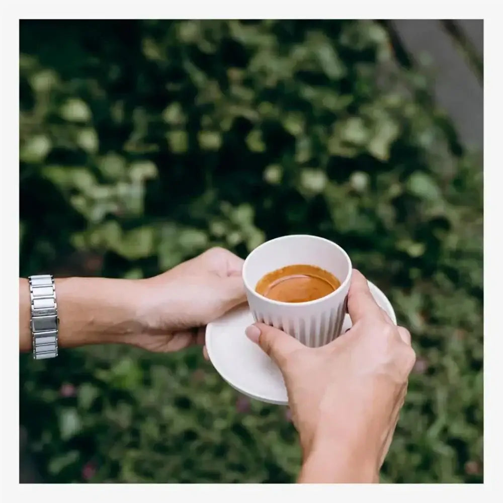 Two hands holding a cup of coffee with a blurred green background