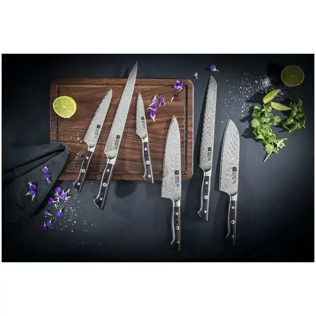 Set of seven Zwilling Takumi Damascus stainless steel knives with black handles arranged on a wooden cutting board