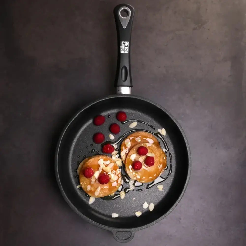 Two pancakes with raspberries and syrup in a frying pan on a dark surface