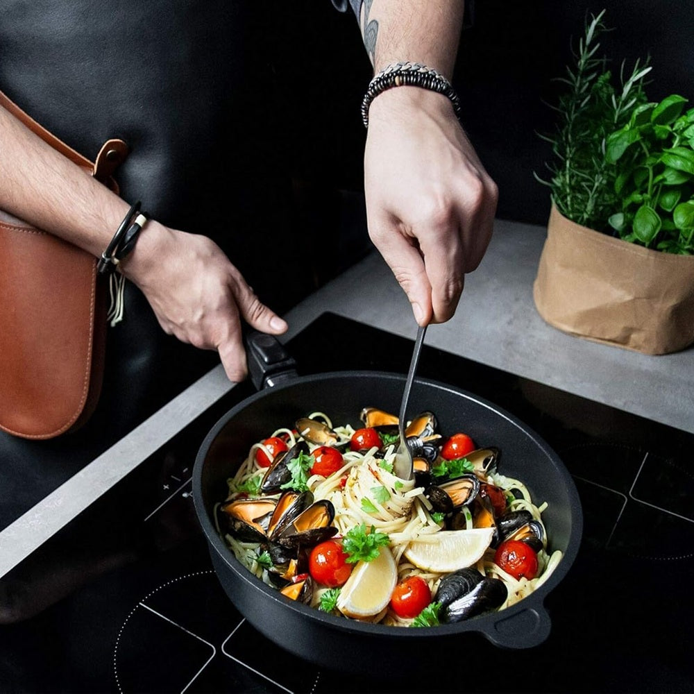 Person cooking a dish with mussels and vegetables in a pan on a stove.
