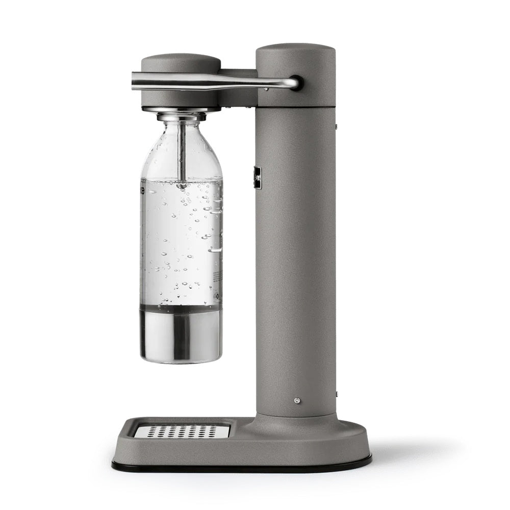 Dark grey water carbonator with a clear glass bottle attached on a white background