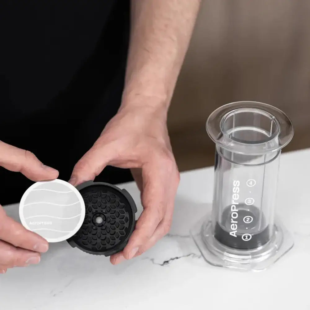 Person assembling an AeroPress coffee maker on a marble surface