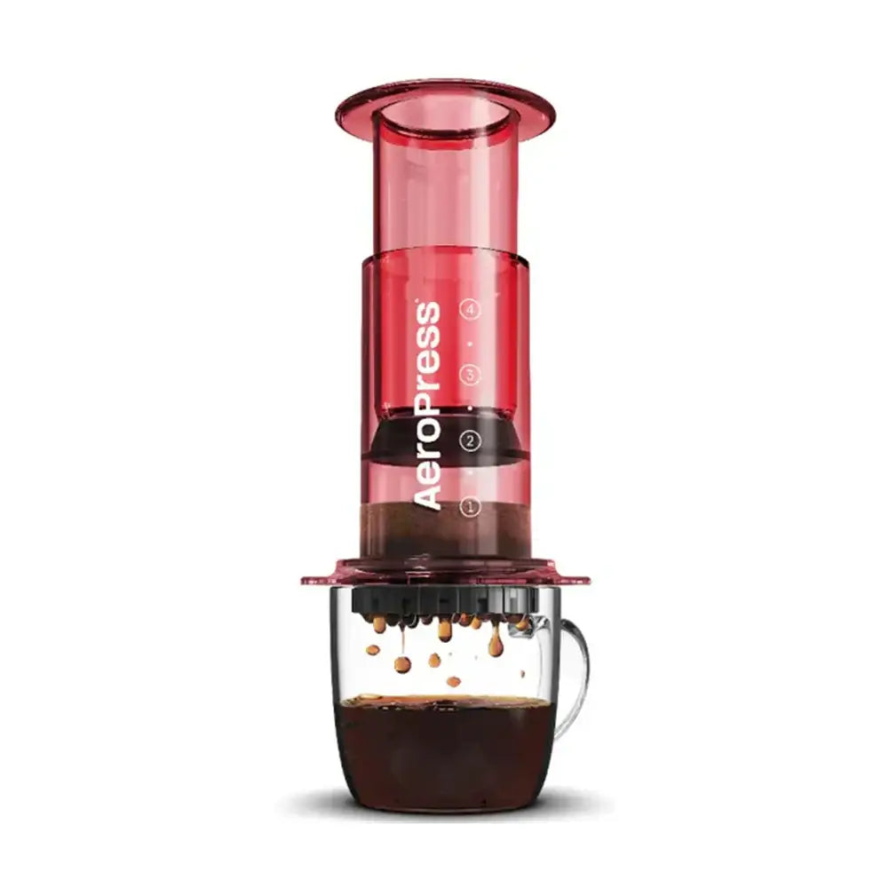 Red Aeropress coffee maker with a glass of coffee on a white background