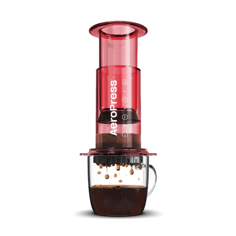 Red Aeropress coffee maker with a glass of coffee on a white background
