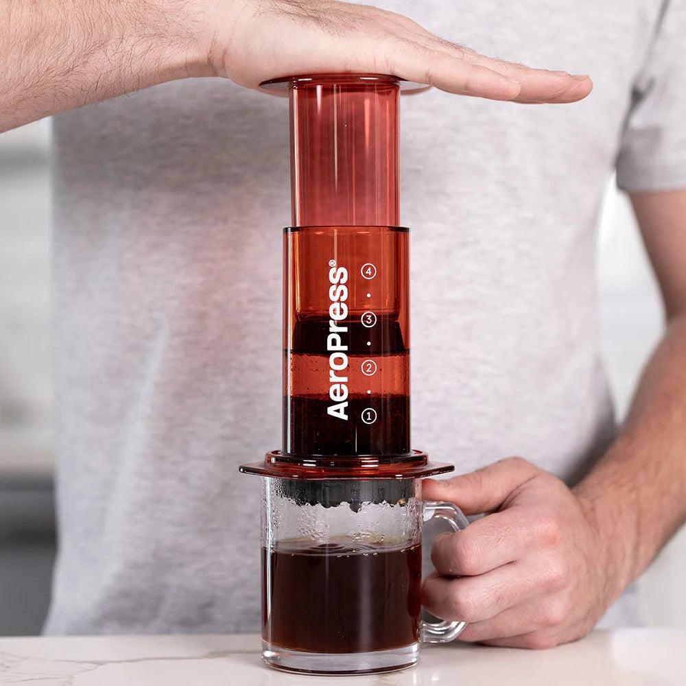 A person using an Aeropress coffee maker with a glass of brewed coffee.