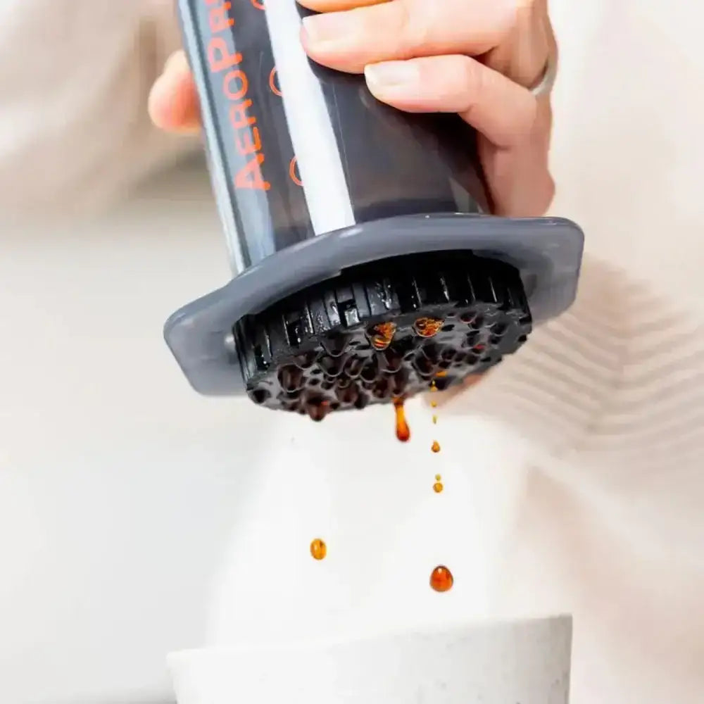 A person using an Aeropress to make coffee with coffee grounds and liquid visible.
