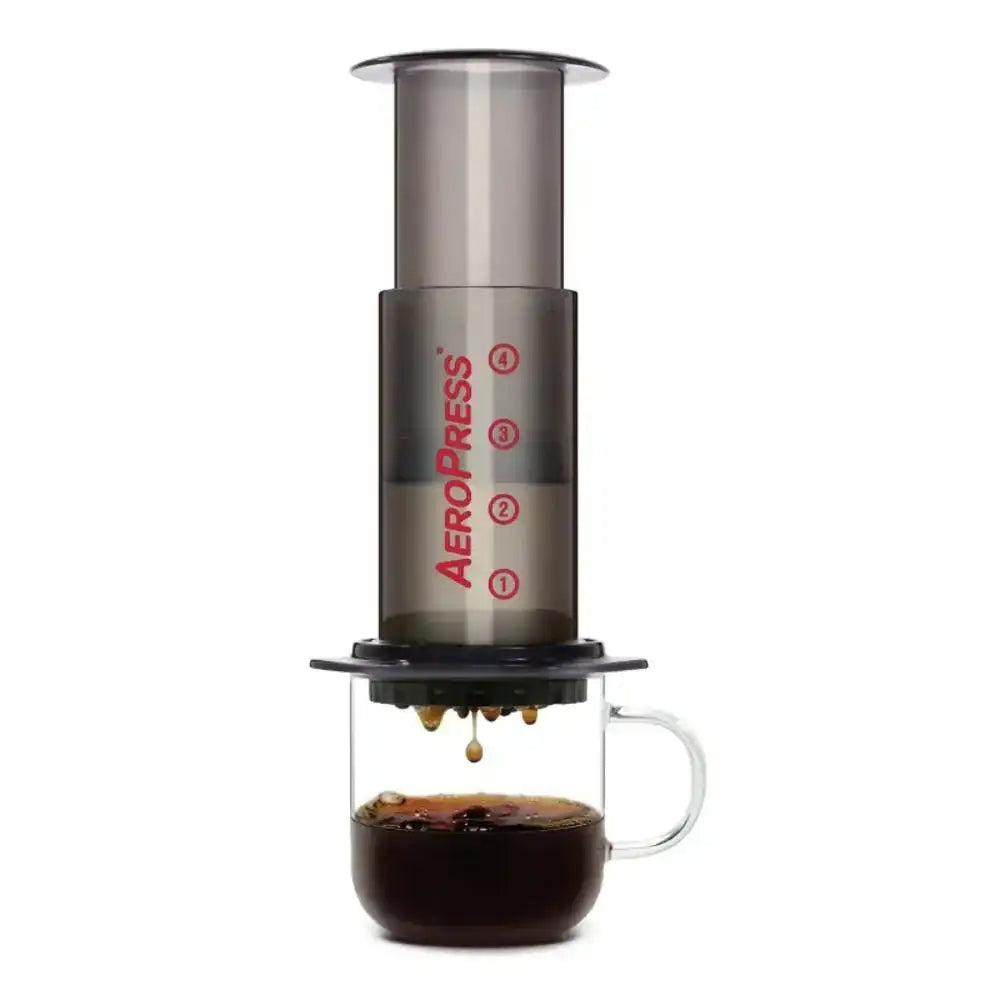 AeroPress Original coffee maker brewing coffee into a glass cup on white background