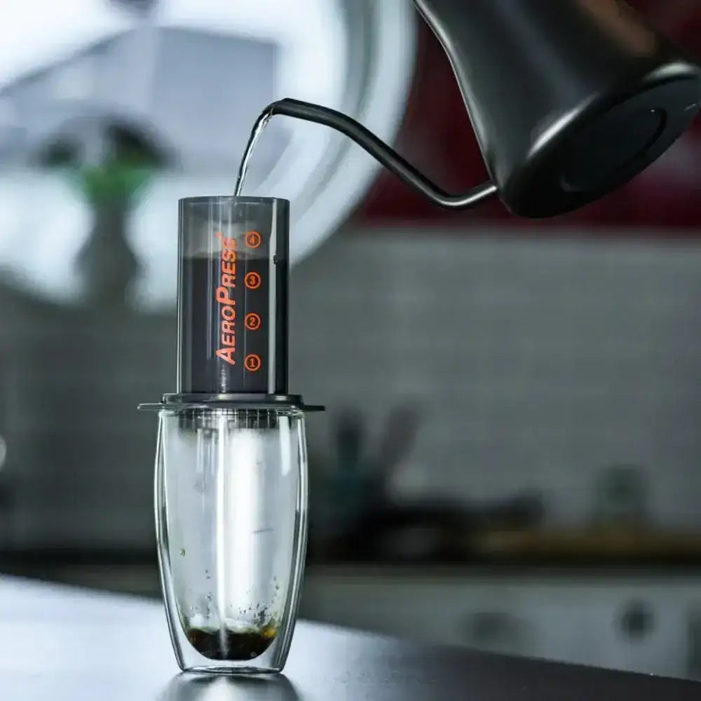 AeroPress coffee maker being used to make coffee with a blurred kitchen background