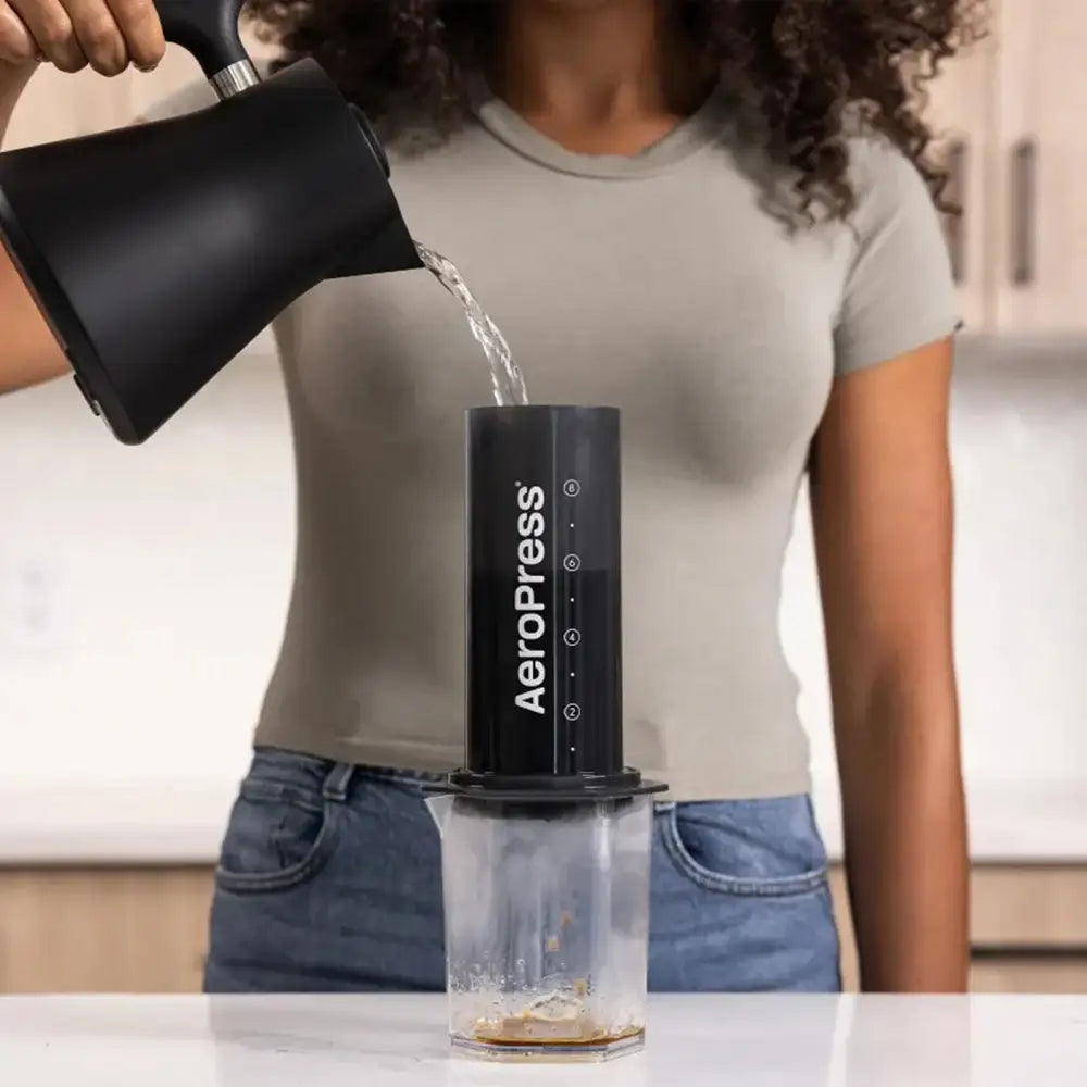 Person using an Aeropress coffee maker with water being poured into it.