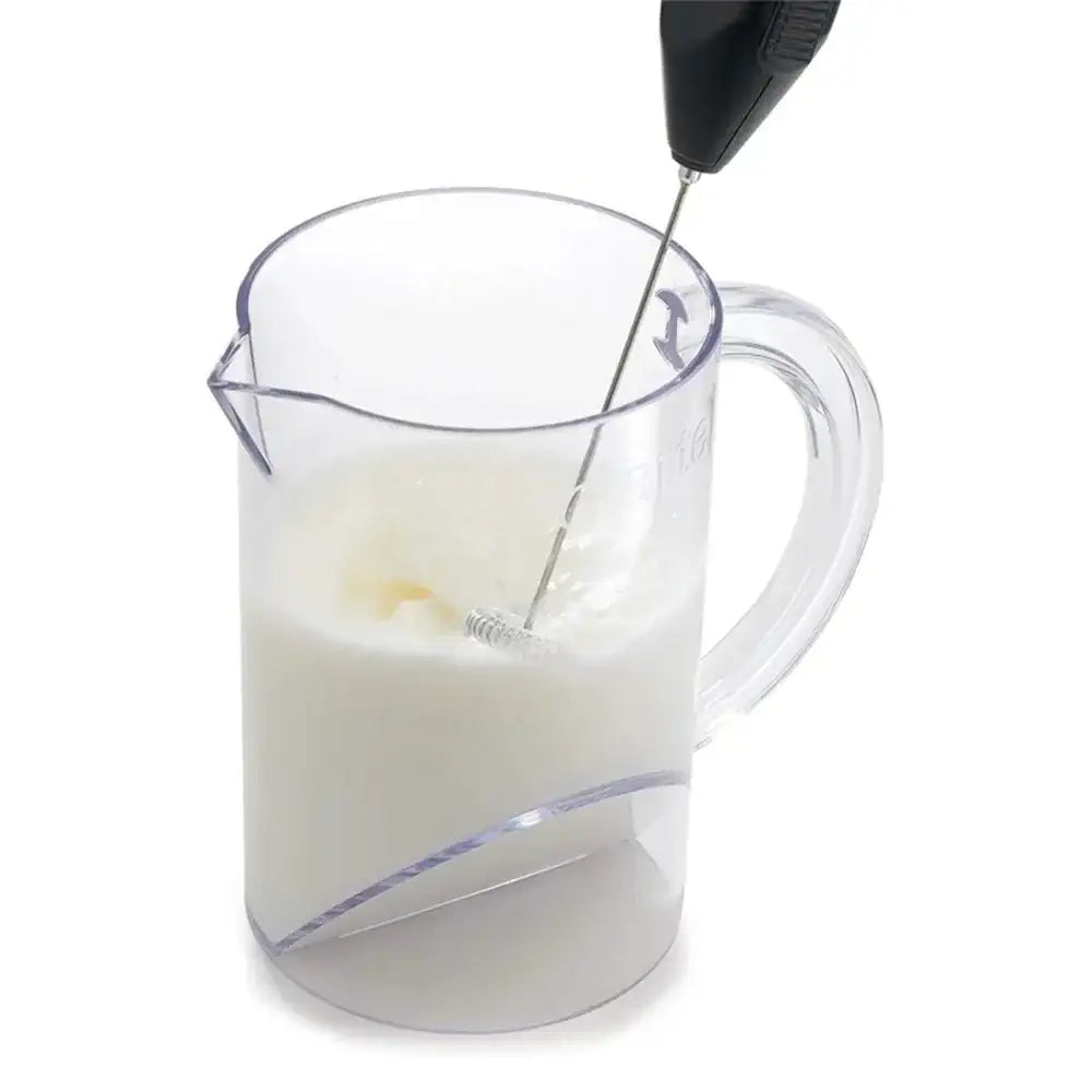 Pitcher of milk being stirred with a hand mixer on a white background