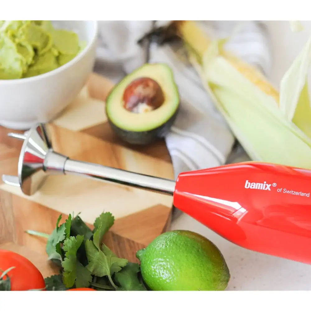 Bamix blender on a table with ingredients including an avocado, lime, and a bowl of guacamole.
