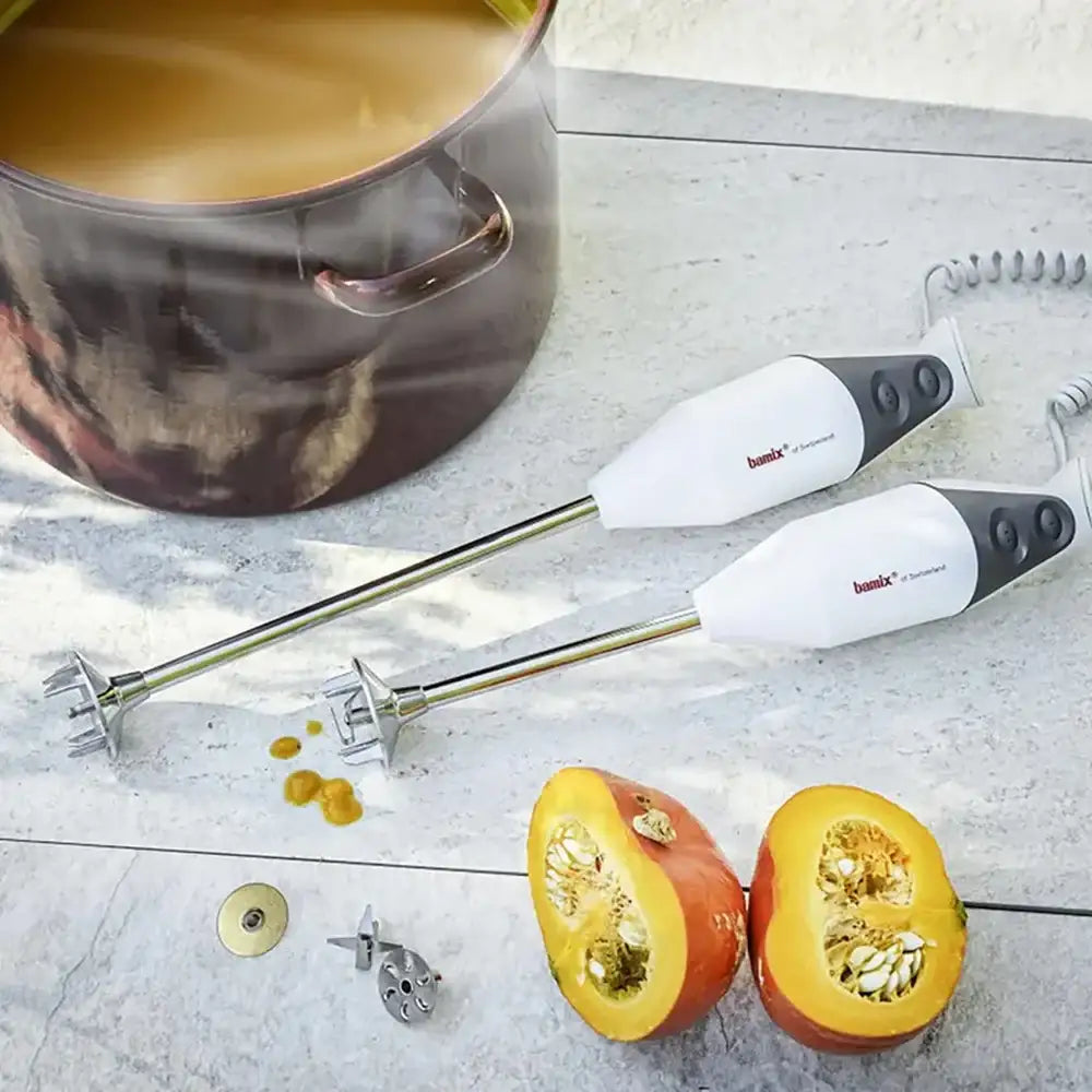 Two hand mixers on a kitchen counter with a pot of soup and halved pumpkin.