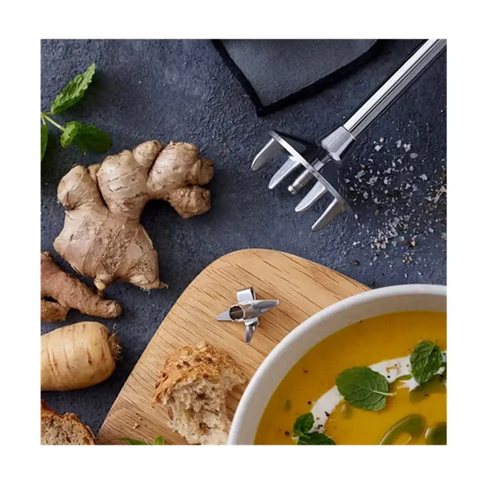 Ginger root, bread, and a bowl of soup on a dark surface with a wooden board.