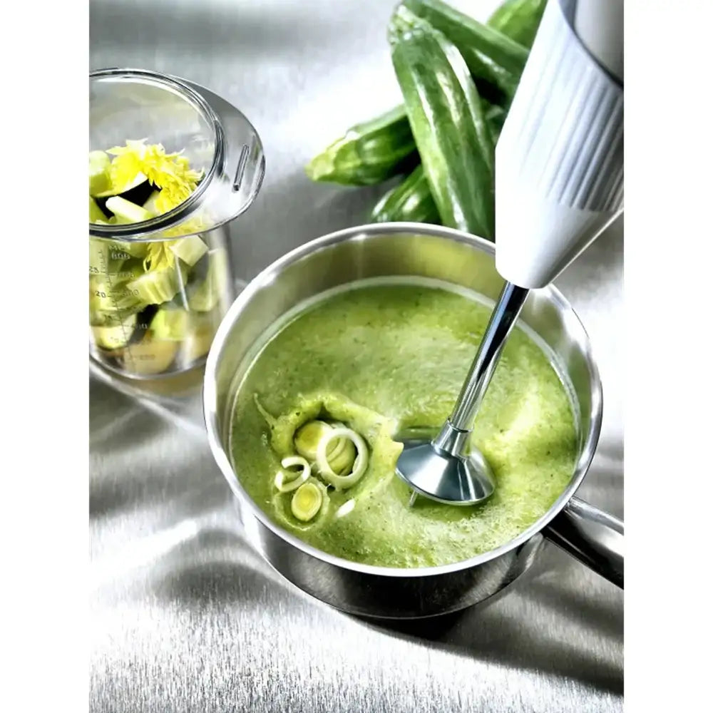 Green soup in a metal pot with a blender on a reflective surface