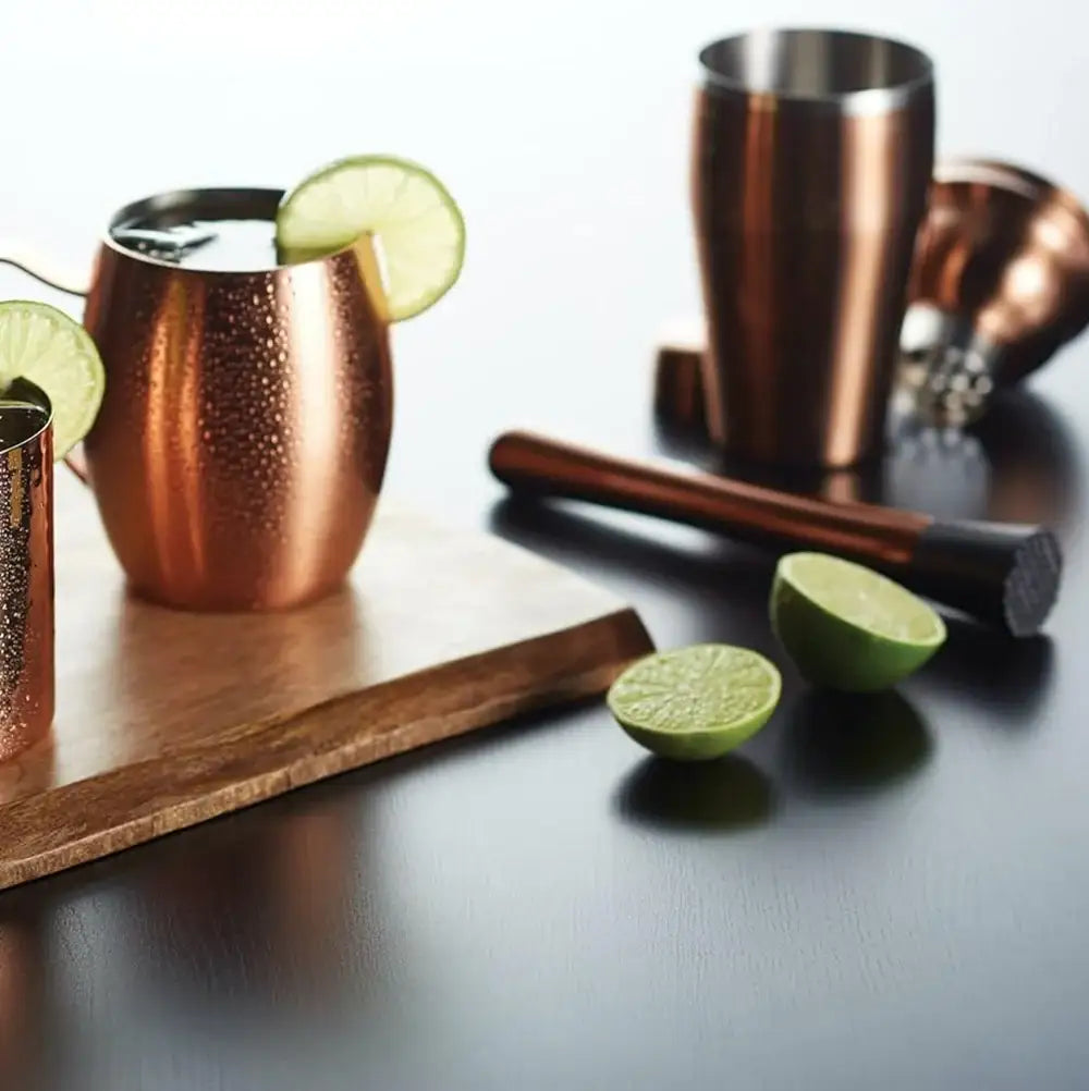 Copper mugs with lime wedges on a wooden board with a dark surface.