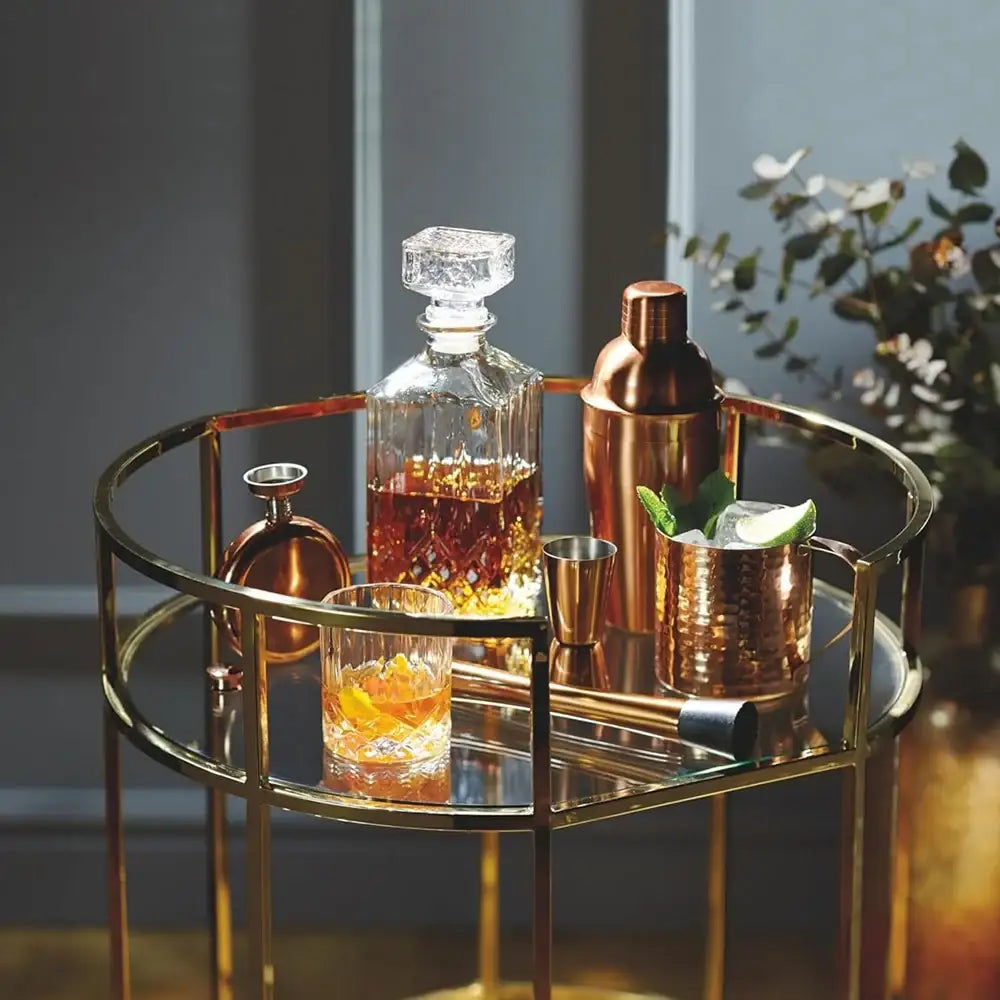 Bar cart with cocktail-making items including a decanter, shaker, and glasses on a gold tray.