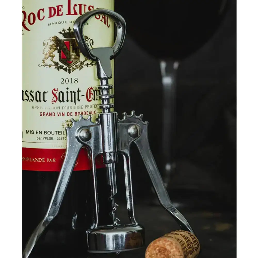 Silver corkscrew in front of a wine bottle labeled 'Roc de Luxe' with a cork on a dark background.