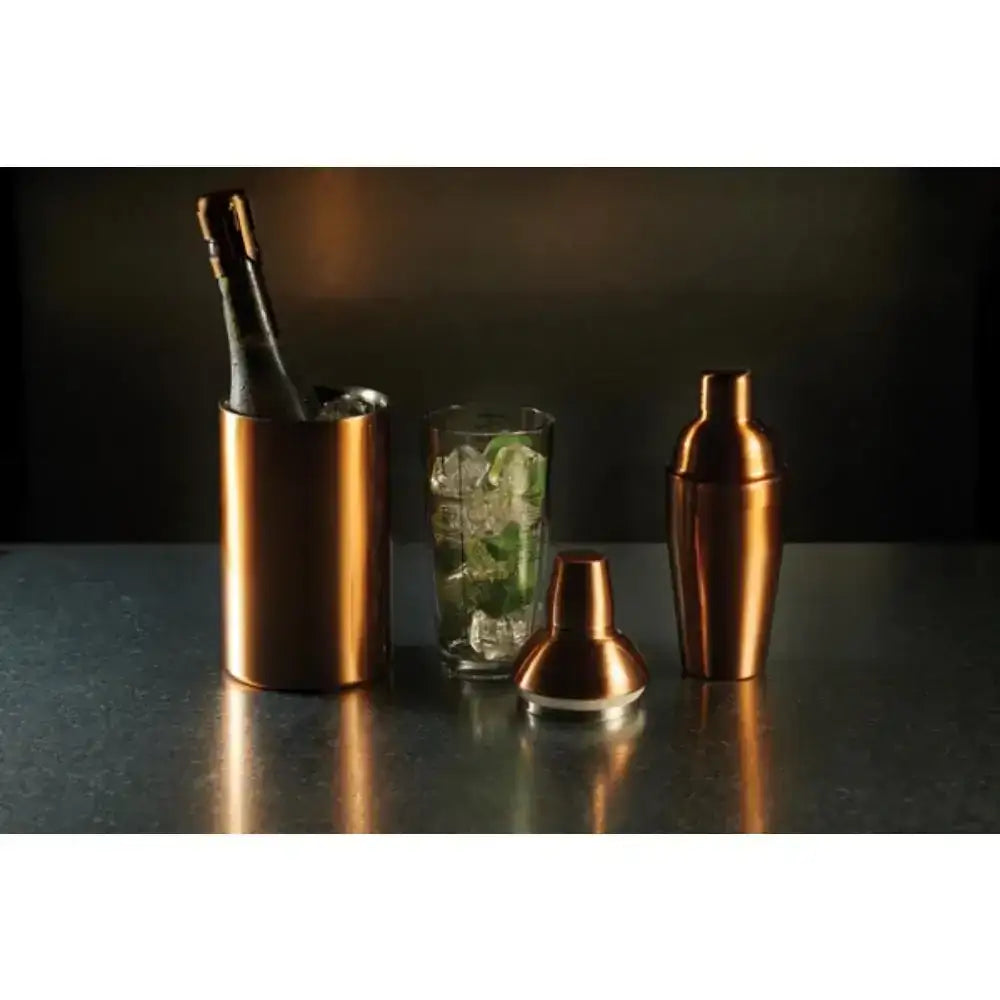 Copper bar tools including a bottle, shaker, and glass on a dark surface.