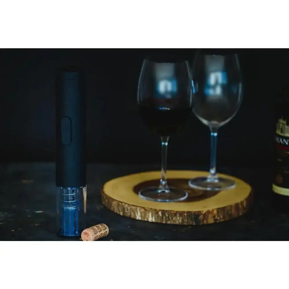 Wine bottle, two glasses, and a cork on a dark surface with a wooden coaster.