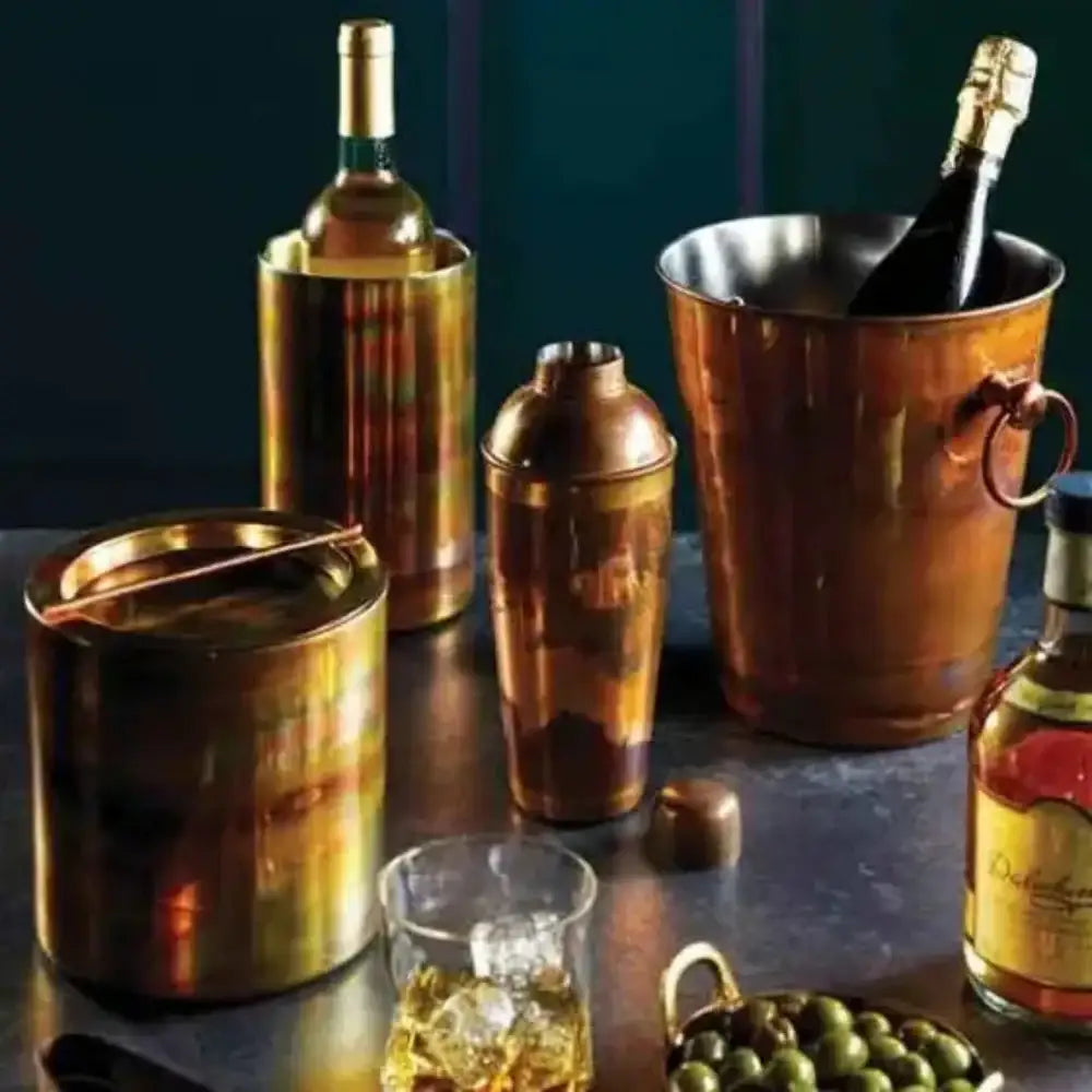 Collection of copper bar tools including ice buckets and a shaker on a dark surface.