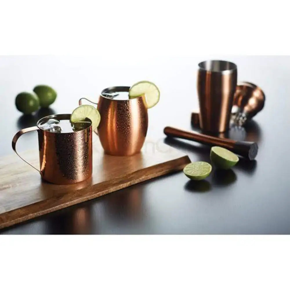 Copper mugs with lime wedges on a wooden board with limes on a reflective surface.
