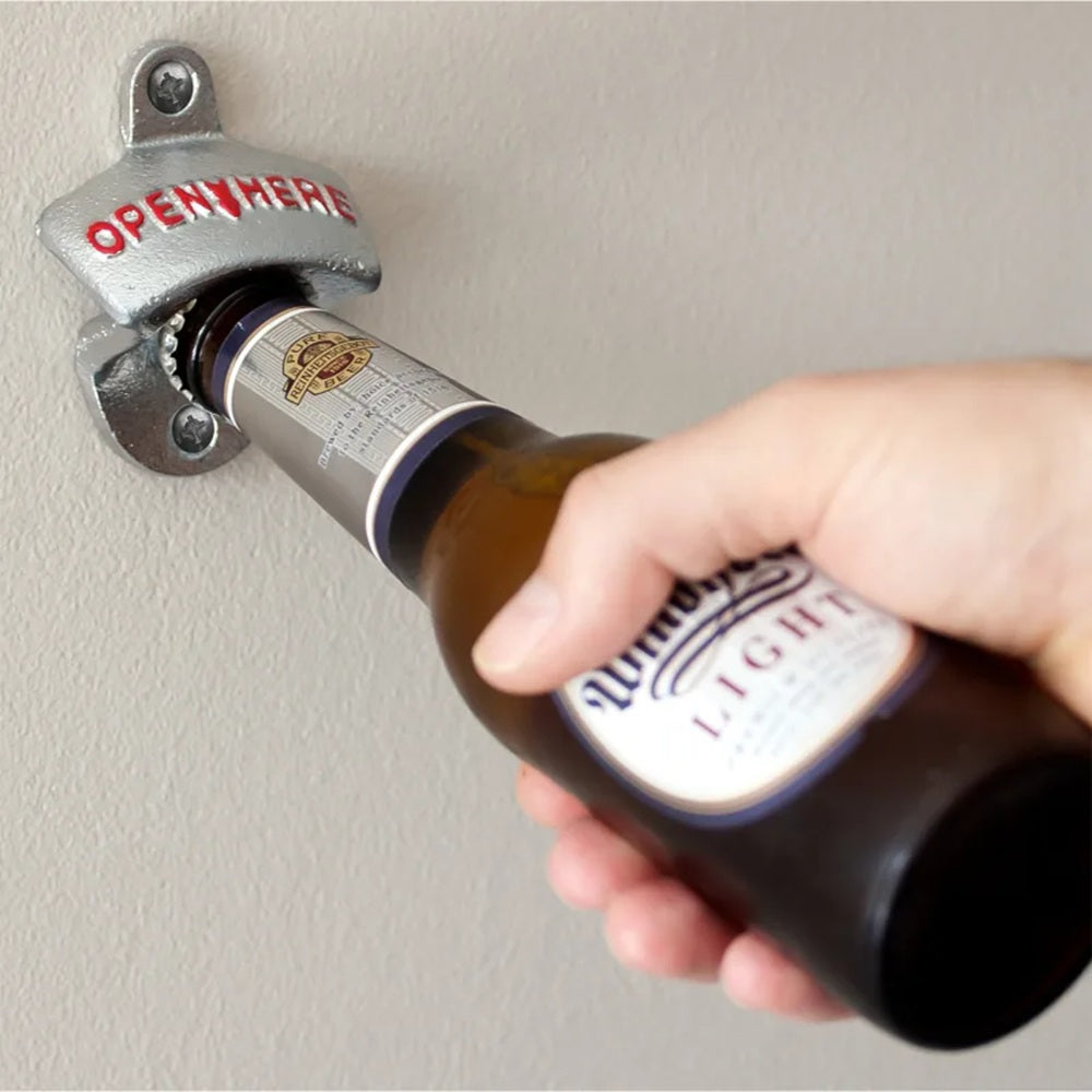 Hand using a wall-mounted bottle opener to open a beer bottle.