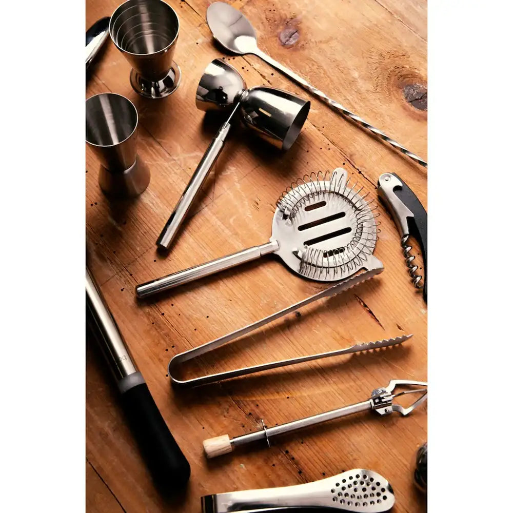 Set of bar tools including jiggers, a muddler, and a strainer on a wooden surface.