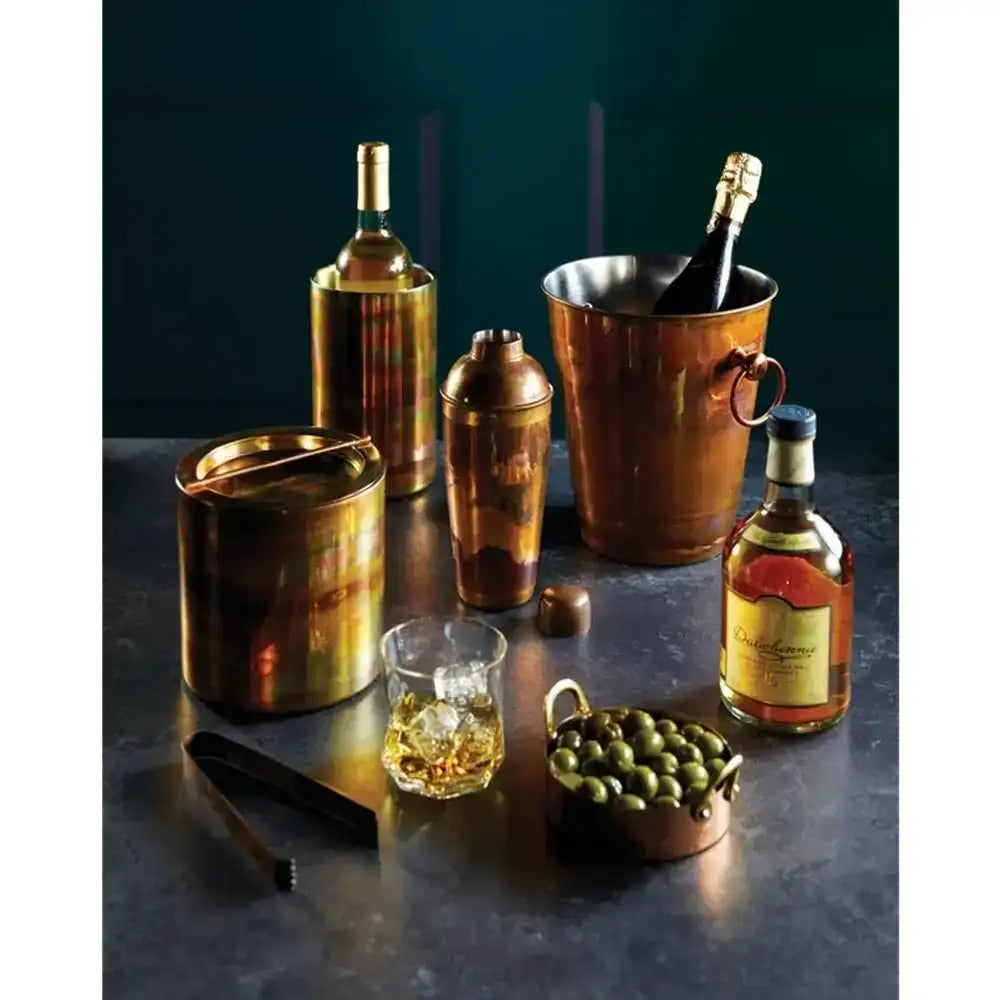 Collection of bronze bar tools and bottles on a dark surface with a dark background