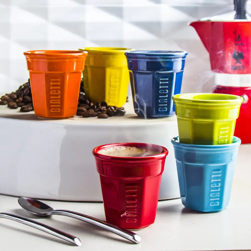 Colorful Cialletti coffee cups on a kitchen counter with coffee beans and a kettle.