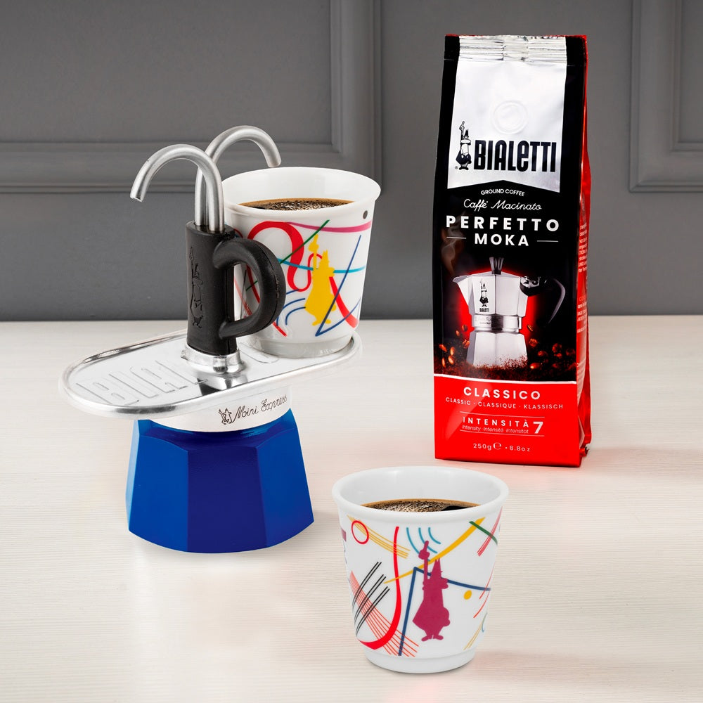 Bialetti Moka Express with two cups of coffee and a package of Bialetti coffee on a light surface.