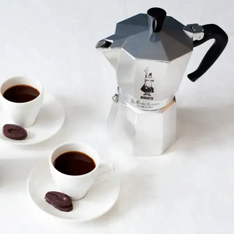 Bialetti Moka Express coffee maker with two cups of coffee on a white background