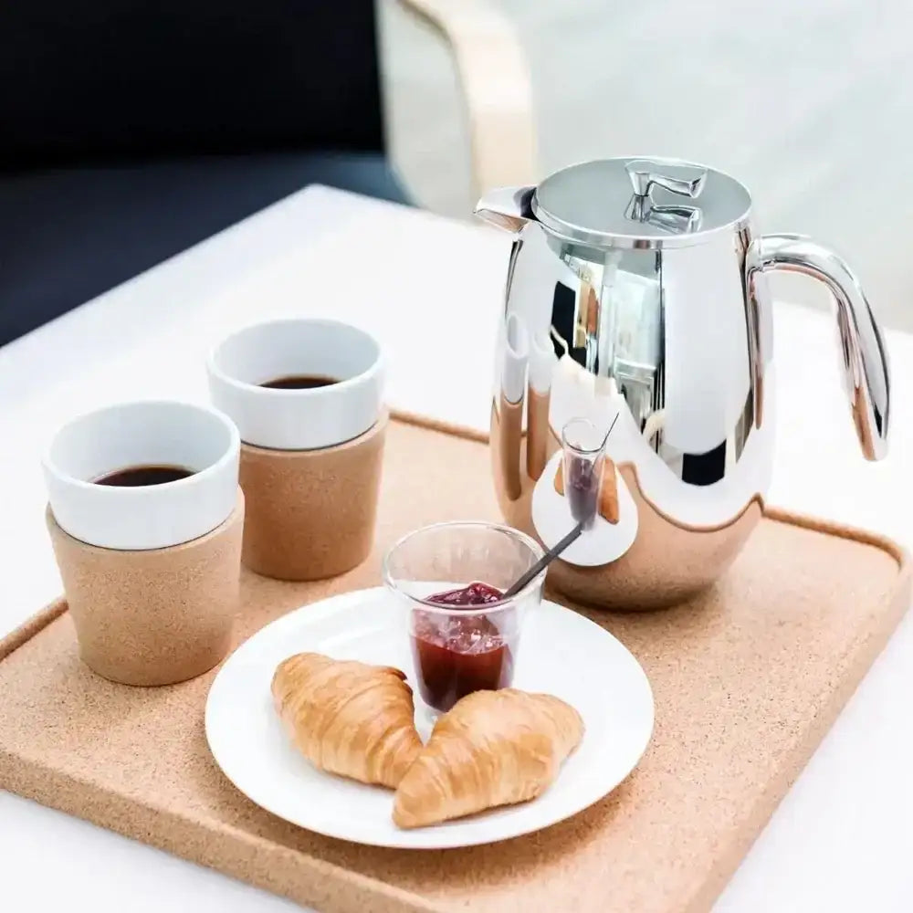 Cork coffee cups with a silver french press, plate of croissants and jam on a tray.