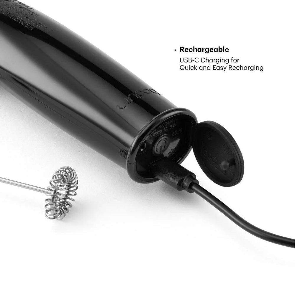 A close-up of a black electric milk frother with its charging port open and connected to a charging cable, alongside a metal whisk attachment. Text on the image reads 'Rechargeable USB-C Charging for Quick and Easy Recharging'.