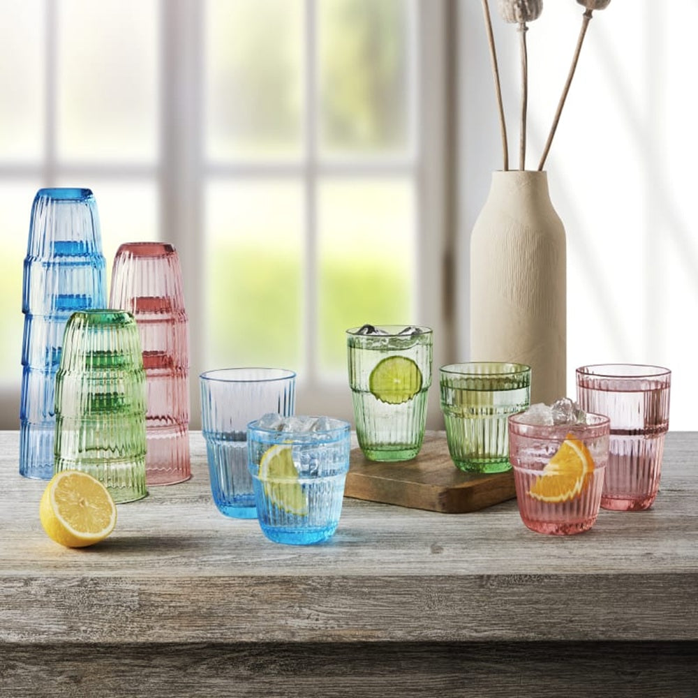 Colorful glass tumblers on a wooden surface with lemons and a vase in the background.