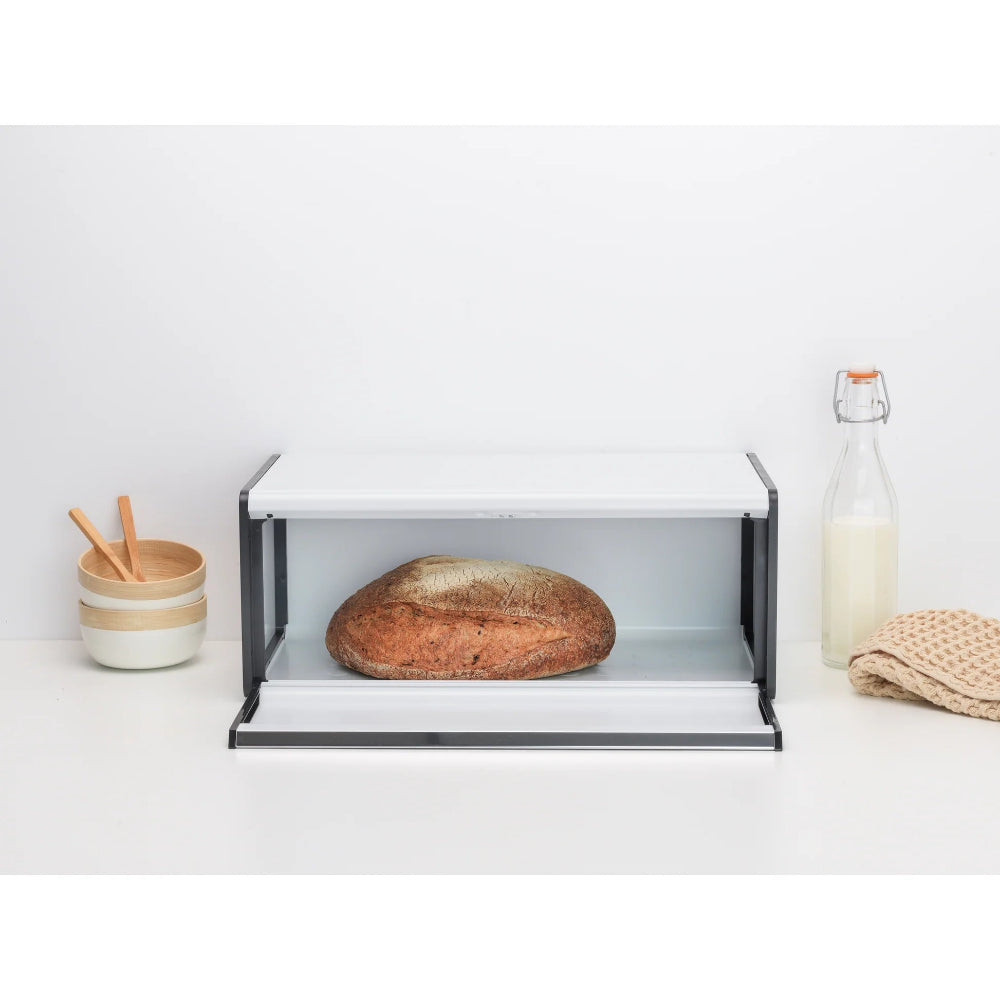 Bread bin with a loaf of sourdough in it, placed on a white kitchen counter.