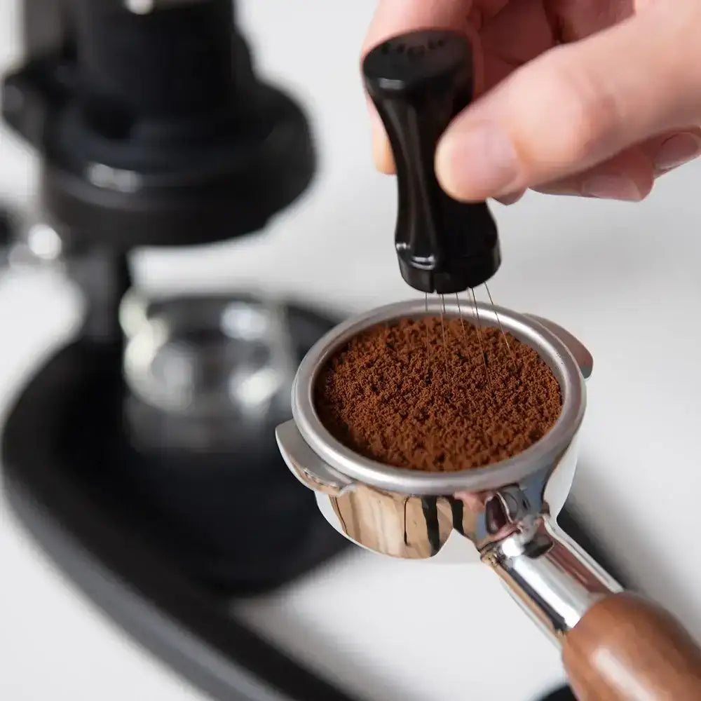 Hand holding a portafilter with ground coffee, blurred coffee machine in the background